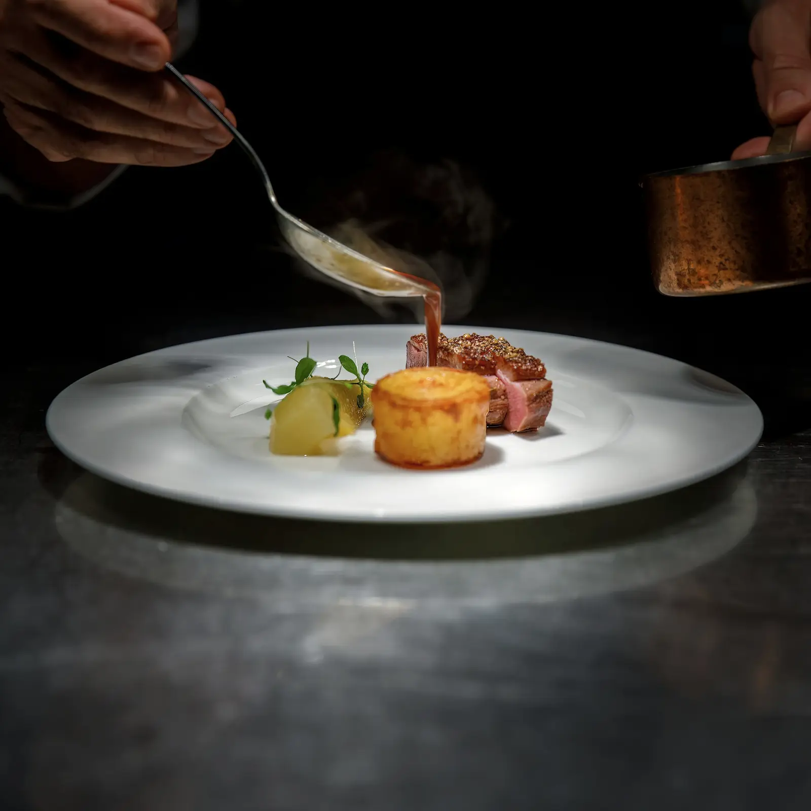 A chef finishing a plated course on a kitchen pass inside a private residence.