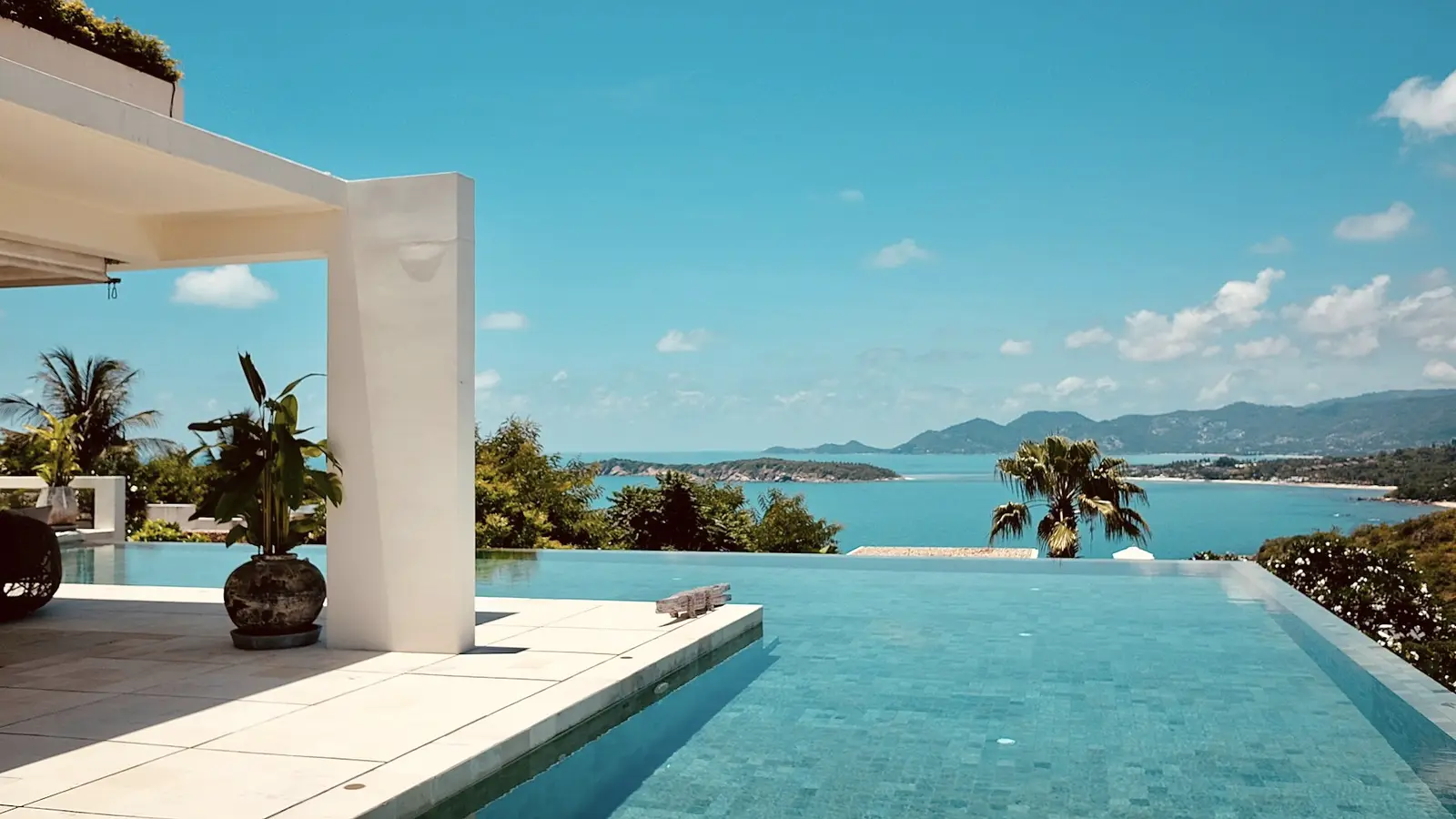 Terrace of a private villa with an infinity pool overlooking the bay at dusk.